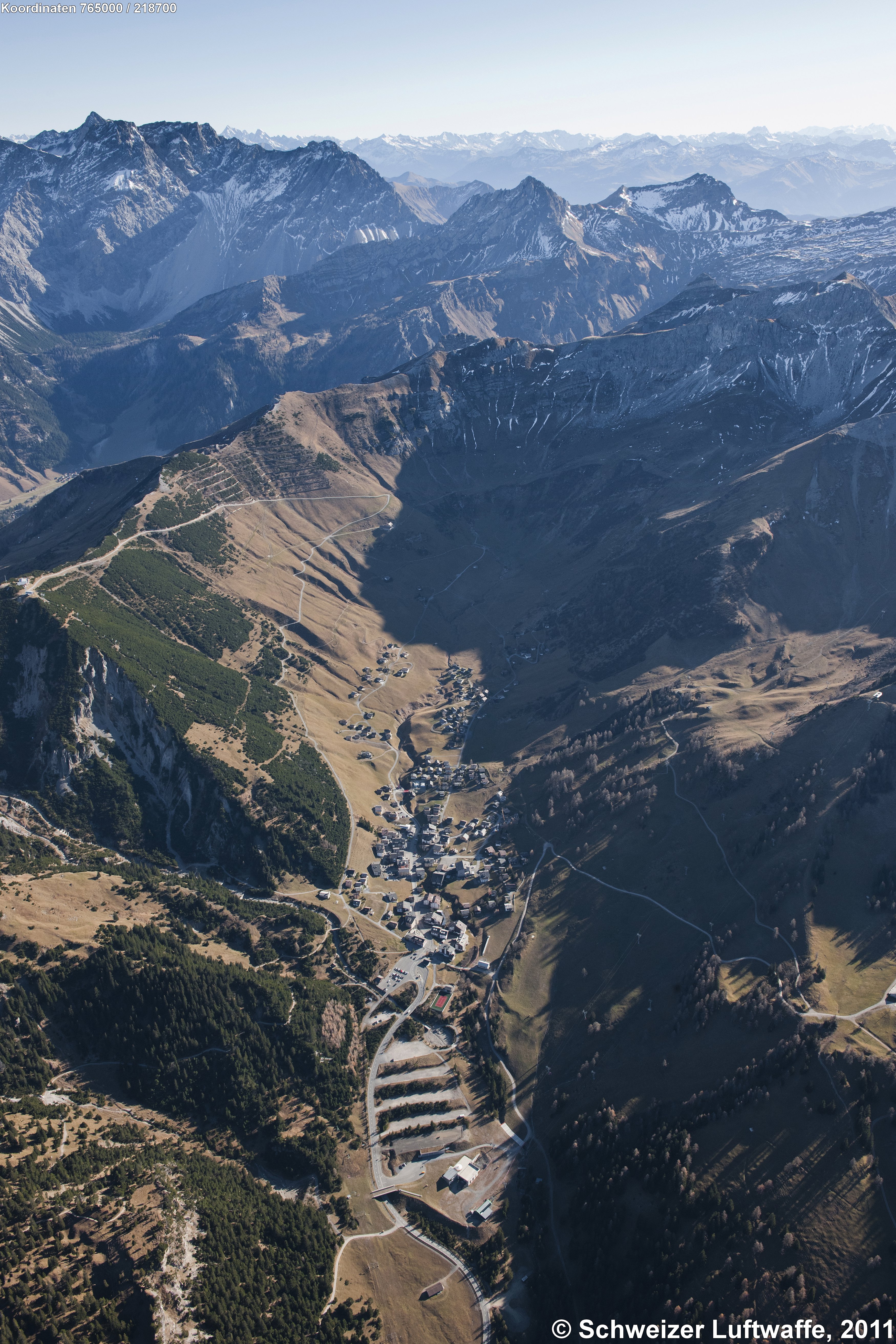 Malbun im Bildzentrum, Blickrichtung SE. - Bergkette links oben im Bild: Schesaplana. Tal im Bildhintergrund: Prättigau. Bildmitte links: Im Chrüz (Sareis), dann Sareiserjoch (mit Lawinenverbauungen), Siedlung im Tal (linker Bildrand): Nenzinger HImmel (Österreich).